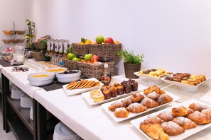A buffet table with various food items including fruits, pastries, and beverages.