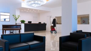 A modern lobby with a reception desk, a grand chandelier, a piano, and comfortable seating areas.