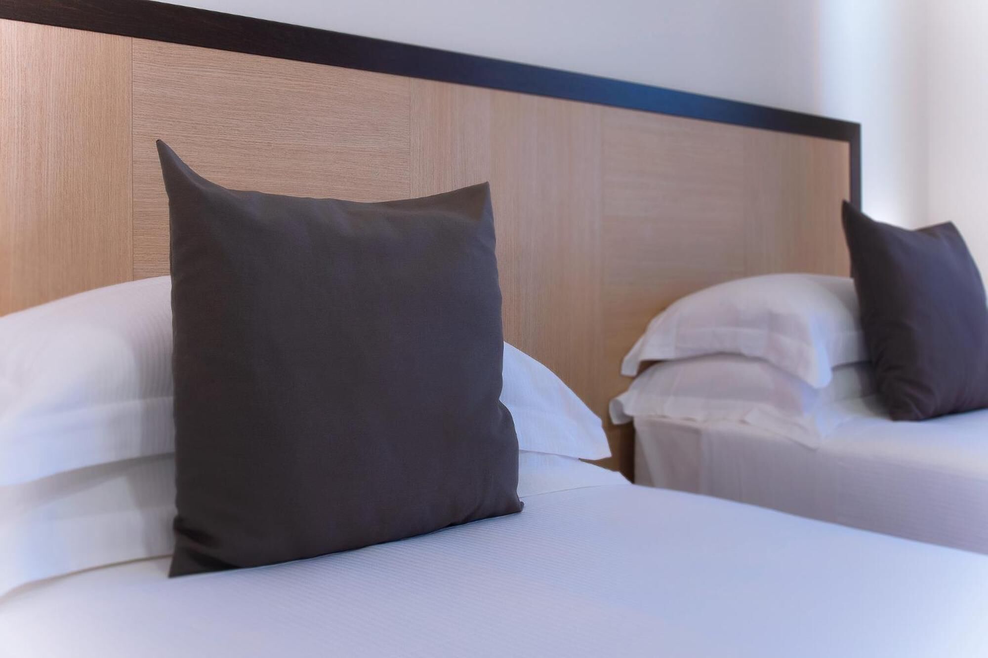 Una camera d'albergo con due letti, ognuno con un cuscino scuro e lenzuola bianche.