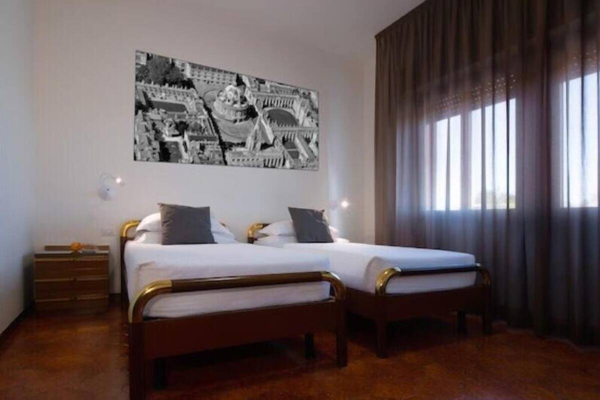 A hotel room with two beds, a large black and white cityscape painting on the wall, and a window with curtains.