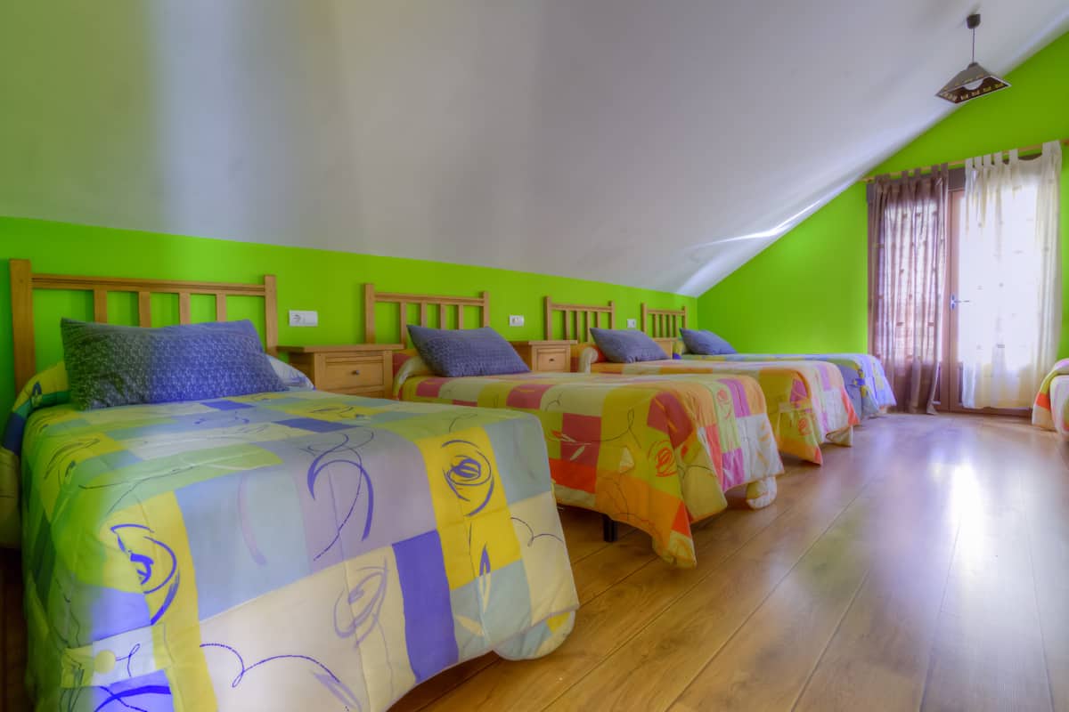 A room with four beds arranged in a row, each with a wooden headboard and a colorful bedspread.