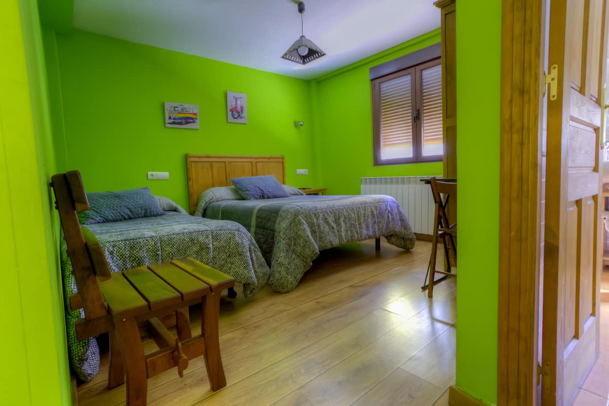 A room with two beds, a wooden chair, a radiator, and a window with blinds.