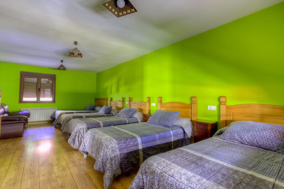 A room with four beds, wooden headboards, a radiator, and a window with blinds.