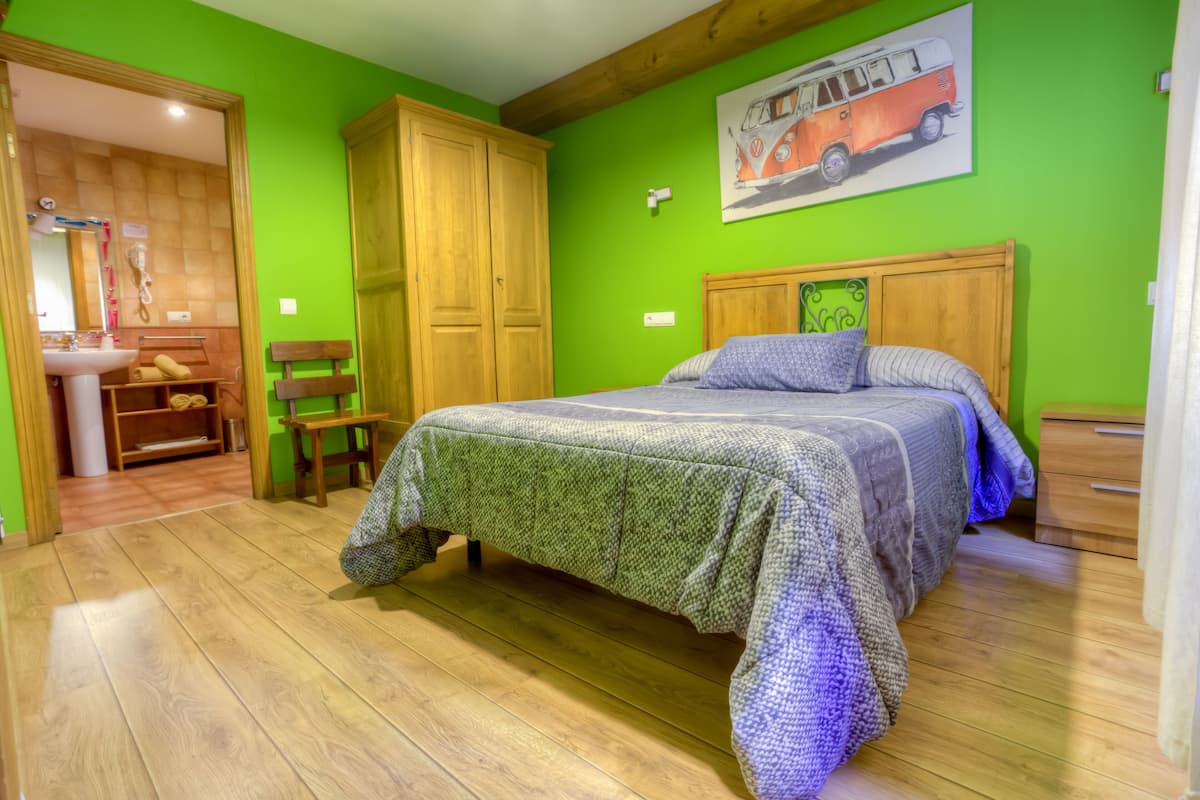 A bedroom with a bed, wooden wardrobe, and a bathroom visible in the background.