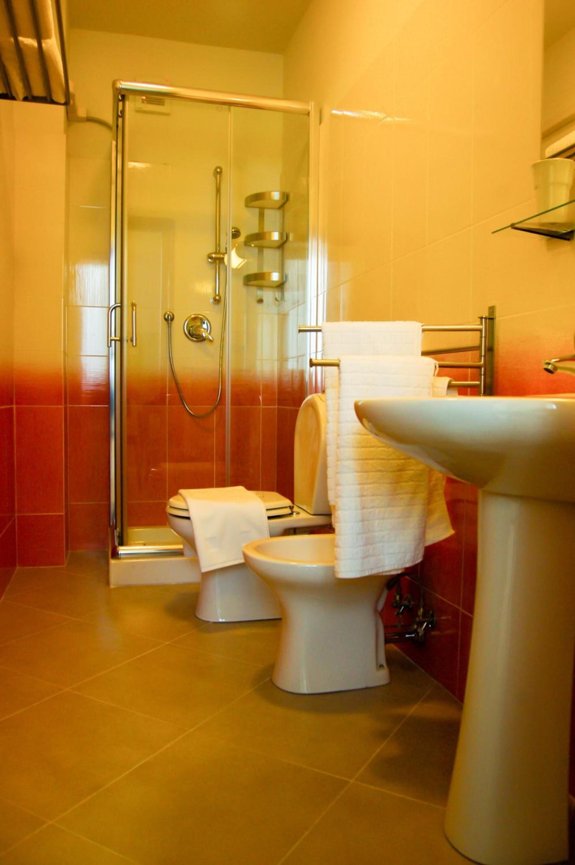 Un baño con ducha envuelta en vidrio, dos inodoros y un lavamanos.