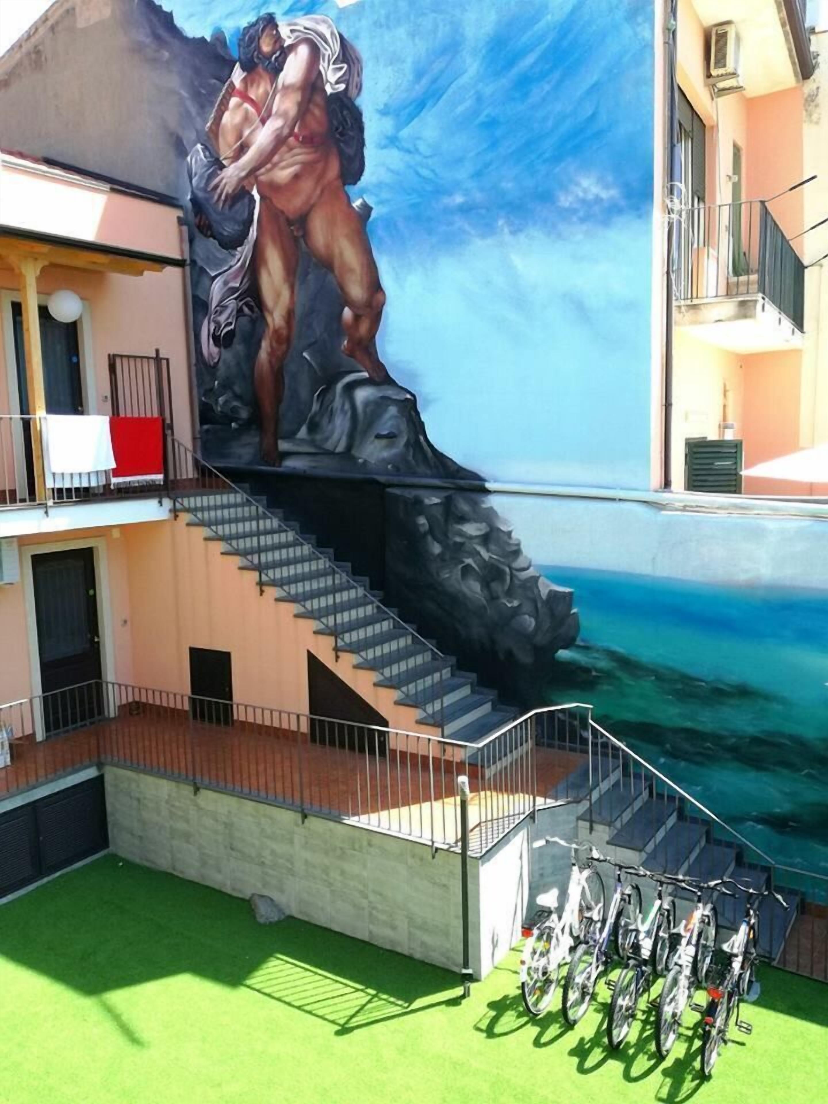 A building with a mural of a muscular man and woman on a staircase. There are bicycles parked outside.