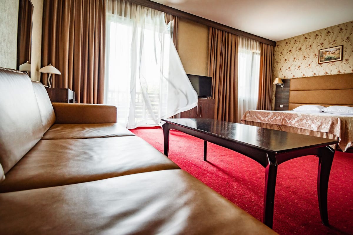 A hotel room with a leather sofa, a small table, a bed with a patterned bedspread, a television, and a painting on the wall.