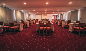 Un salón de conferencias con varias mesas y sillas dispuestas en filas, con alfombra roja y manteles blancos.