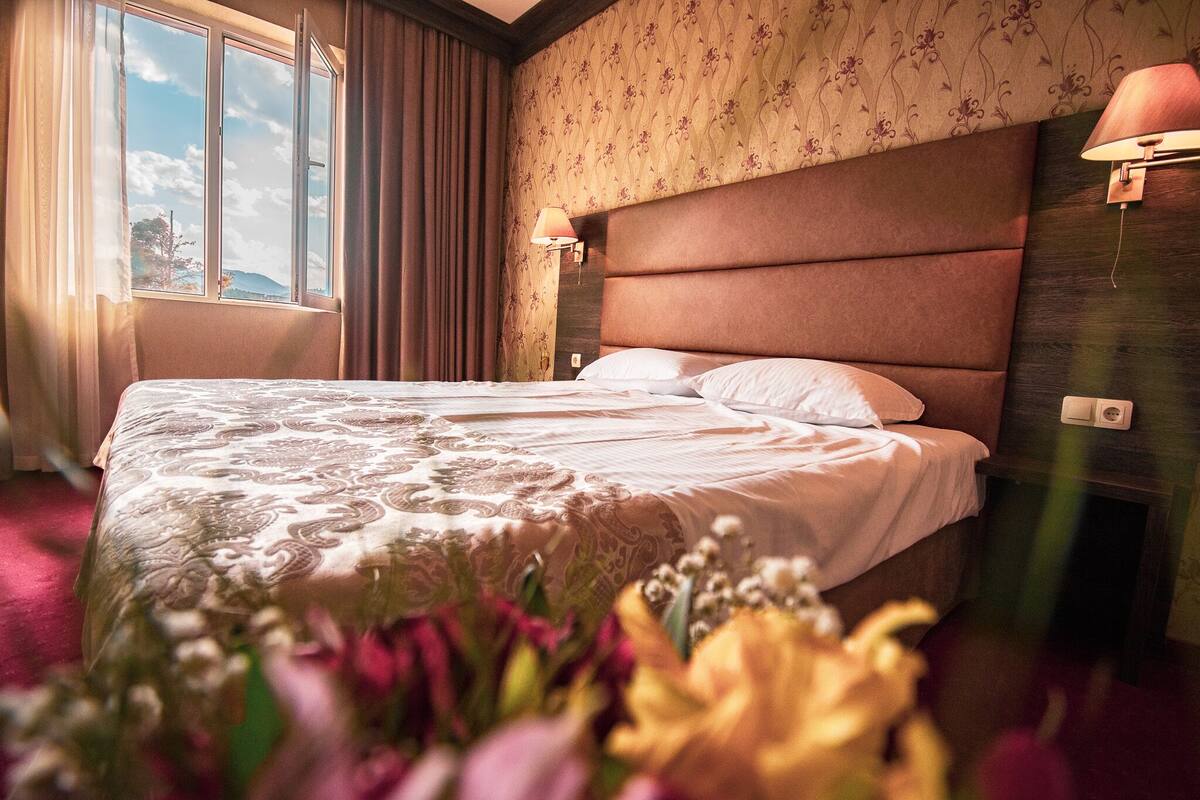 A neatly made bed with a patterned bedspread, a nightstand with a lamp, and a window with curtains.