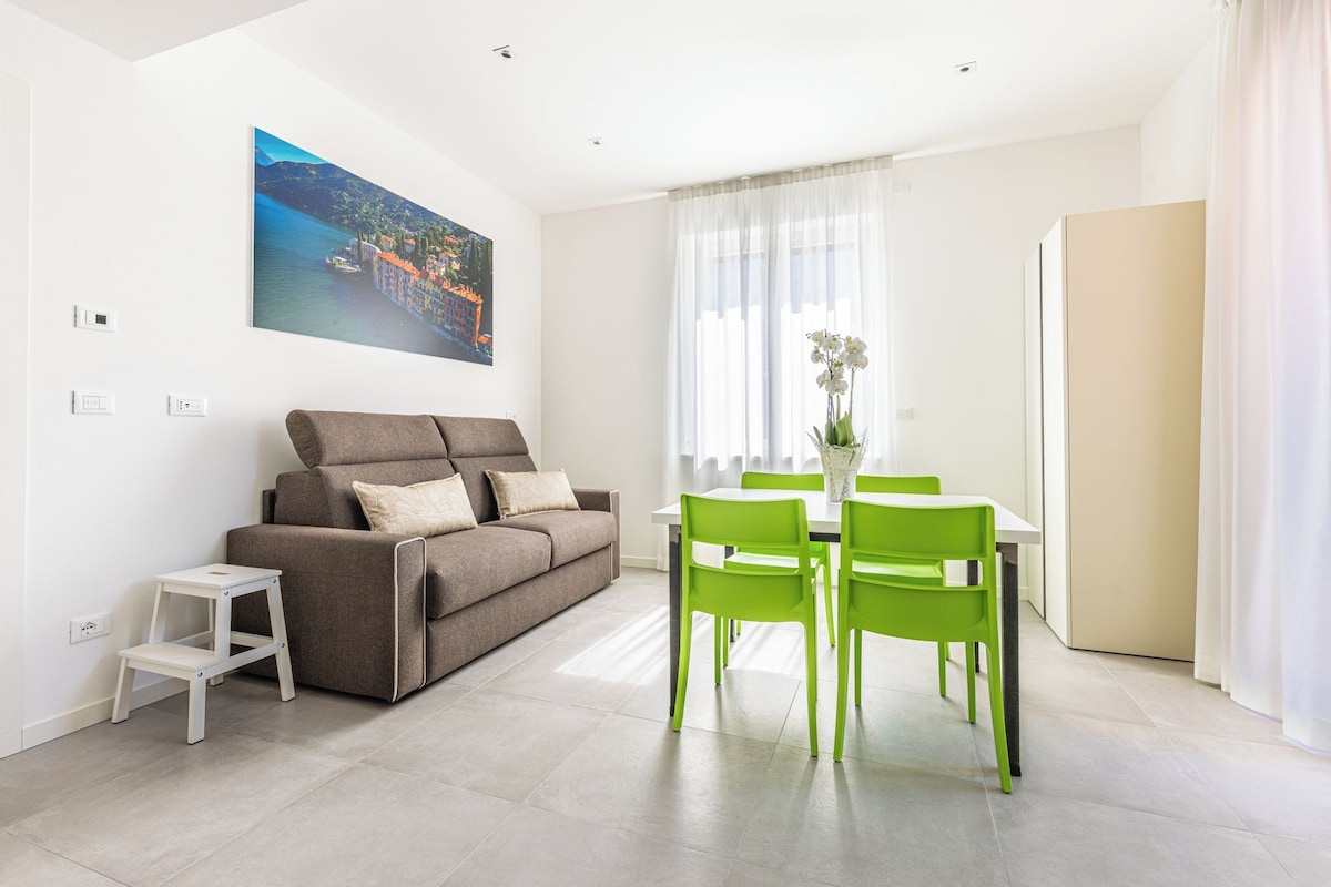 Un salon moderne avec un canapé, une table à manger et des chaises, une petite table d’appoint blanche et un tableau accroché au mur.