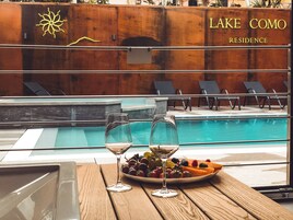 Vista con piscina, sedie a sdraio, un bicchiere di vino e un piatto di frutta.