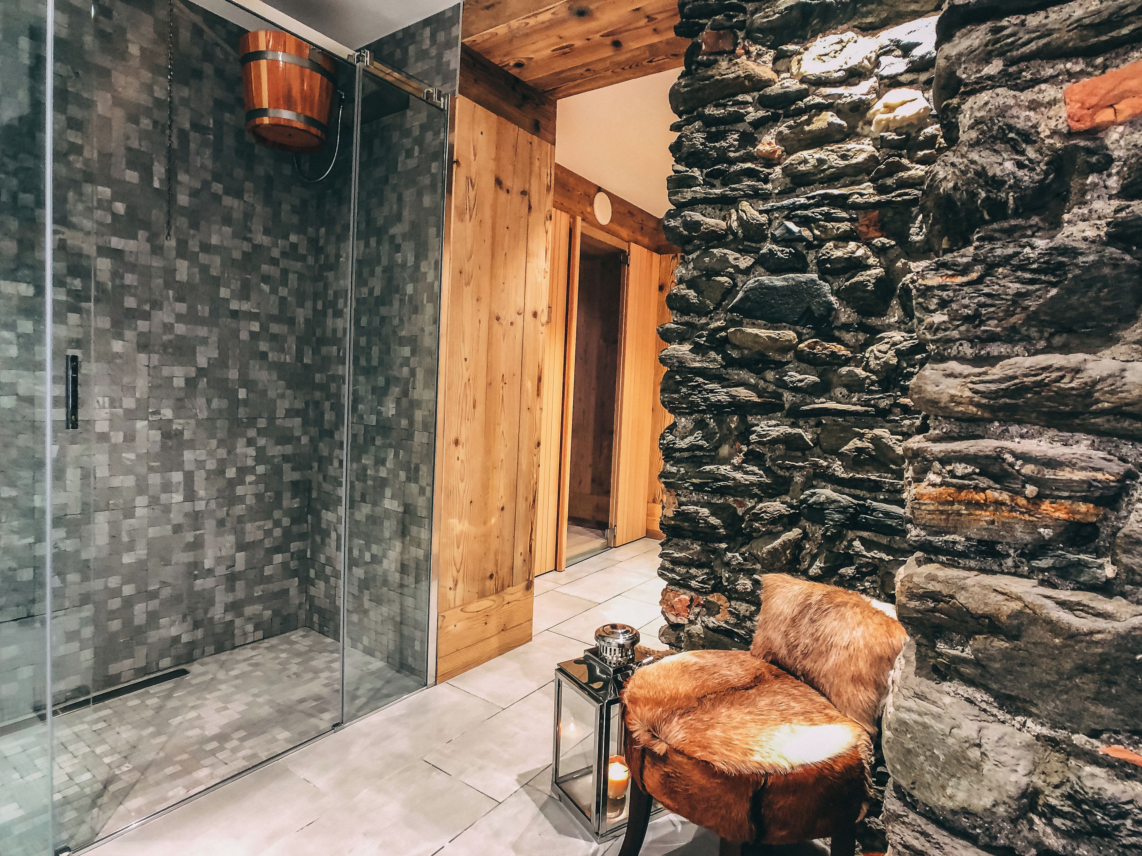 A bathroom with a glass shower enclosure, a wooden door, and a stone wall.