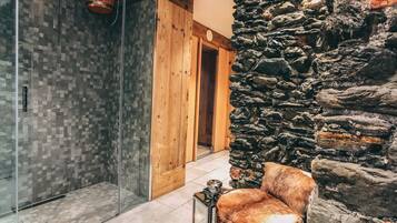 A bathroom with a glass shower enclosure, a wooden door, and a stone wall.