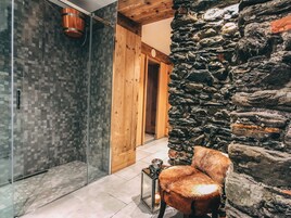 Un baño con cabina de ducha de vidrio, una puerta de madera y una pared de piedra.