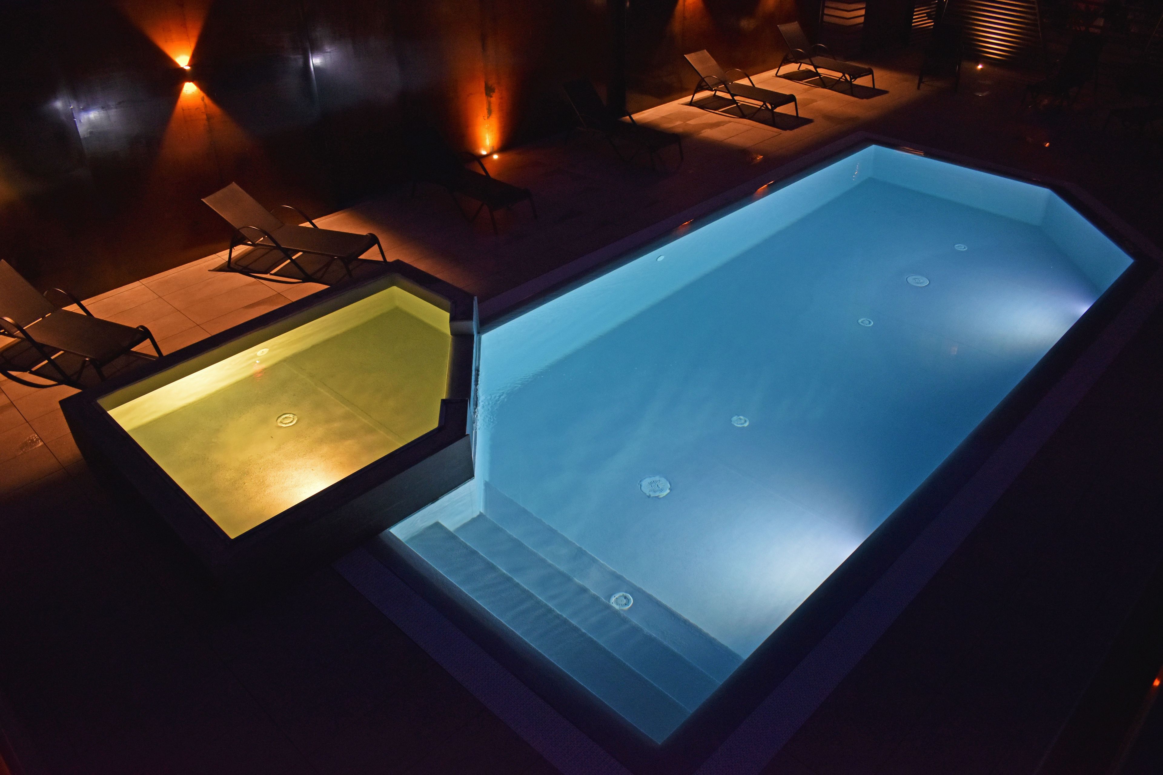 A swimming pool with a glass bottom, surrounded by lounge chairs and a sunbed.