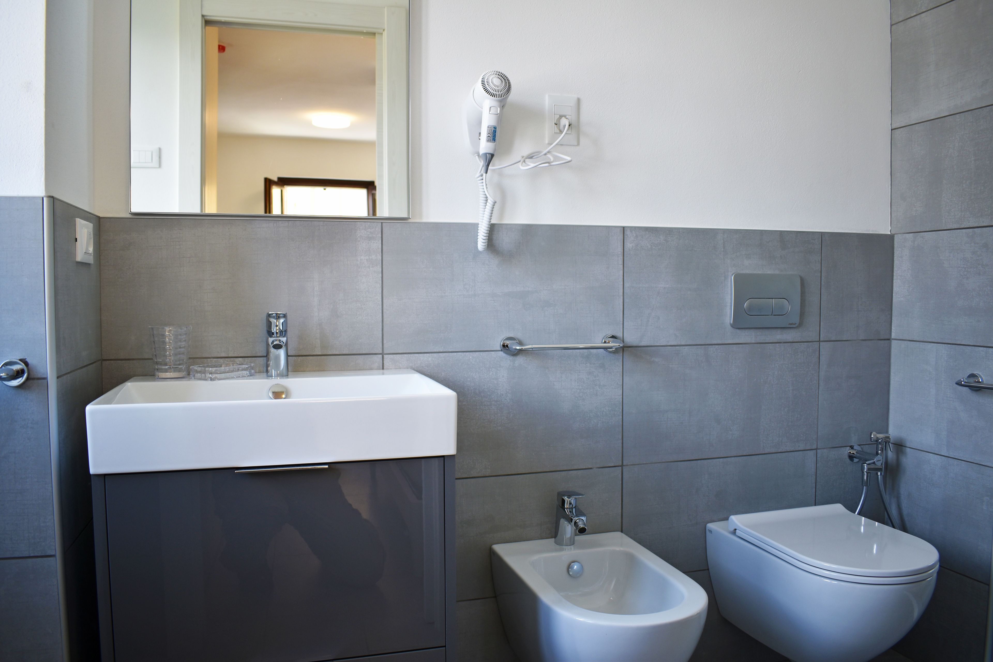 Un baño moderno con lavamanos, bidé y secador de pelo montado en la pared.