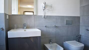 Un baño moderno con lavamanos, bidé y secador de pelo montado en la pared.