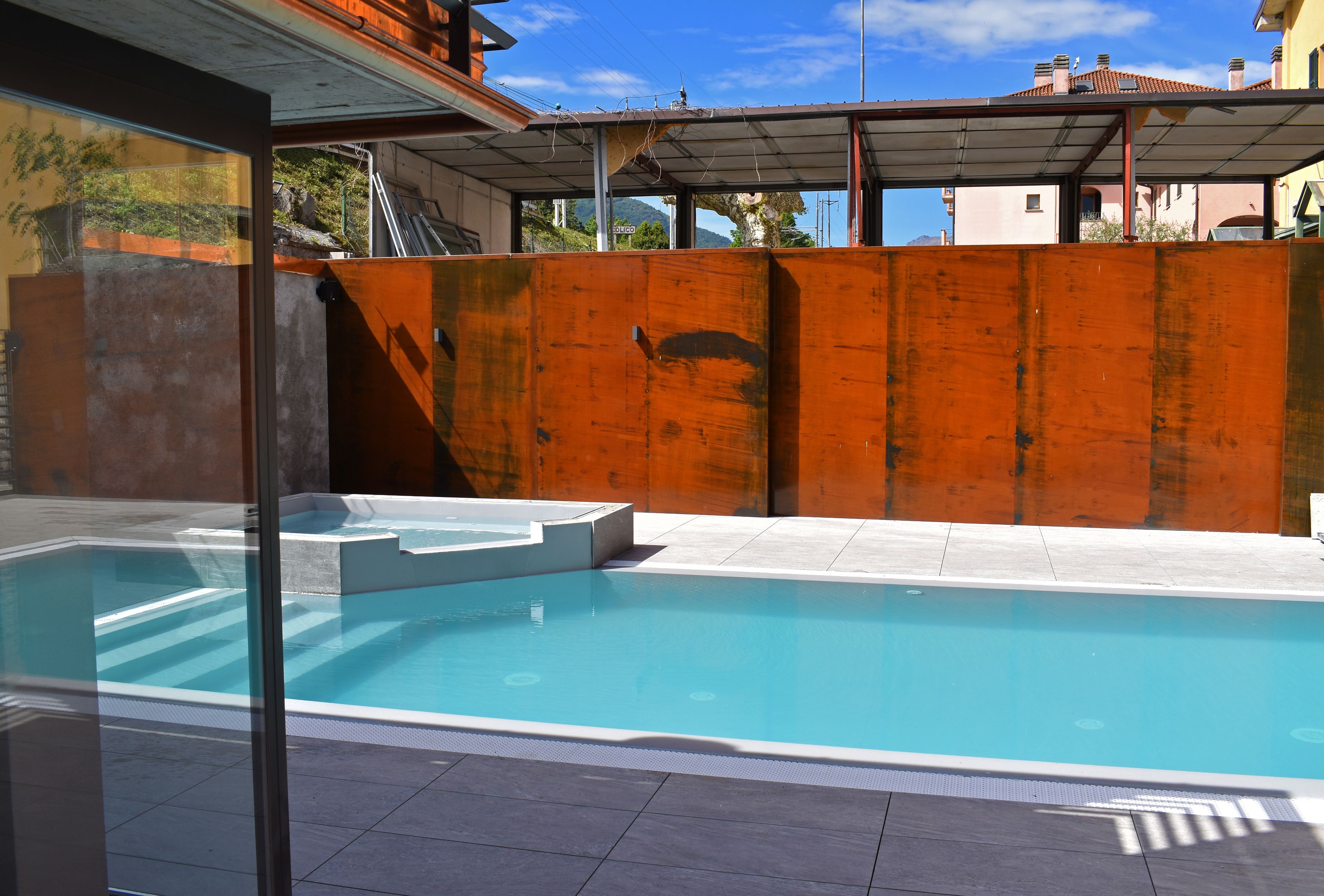 A swimming pool with a clear blue water, surrounded by a wooden fence and a glass wall.