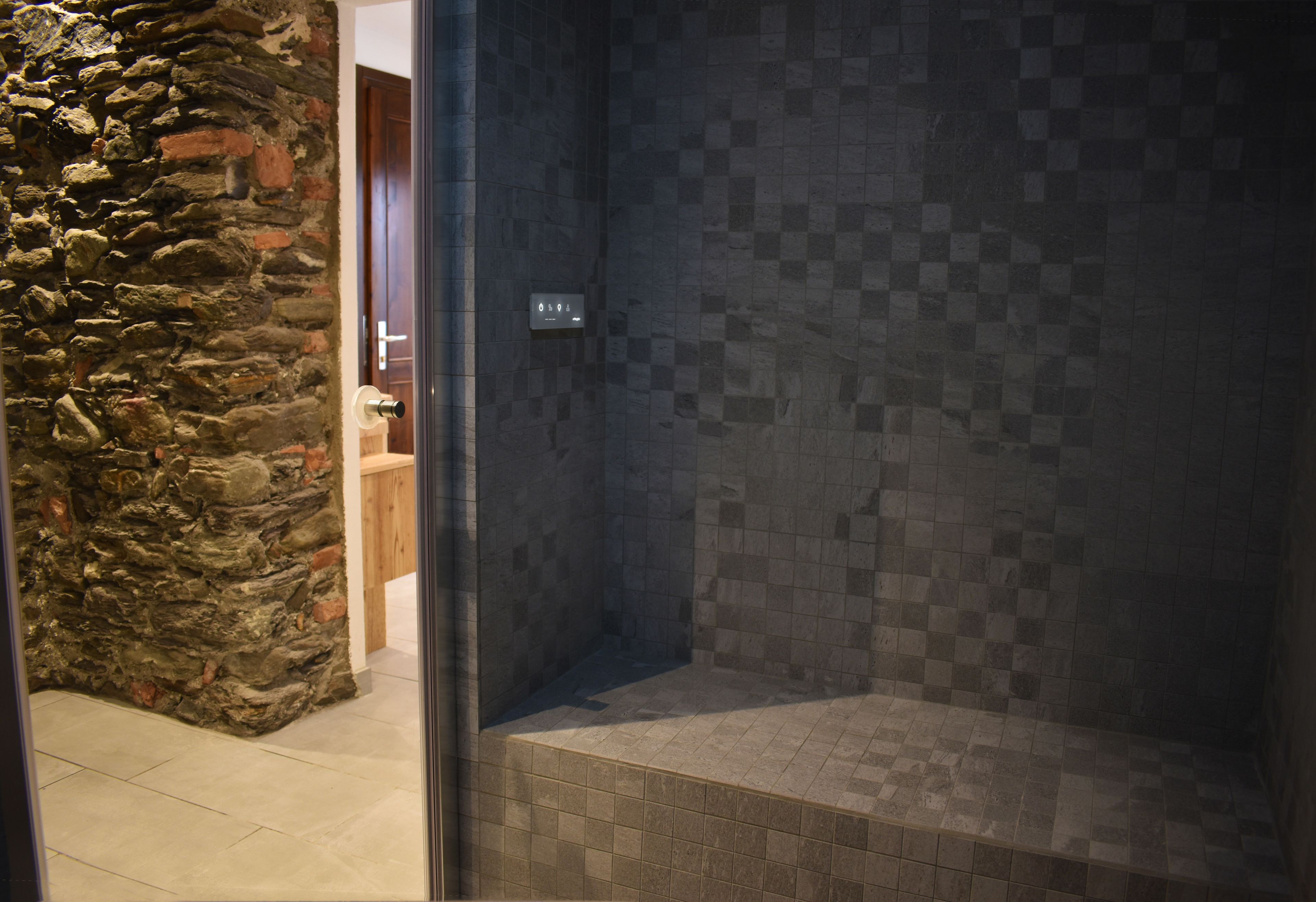 A shower area with a stone wall and tiled floor.