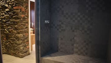 A shower area with a stone wall and tiled floor.