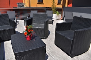 Une terrasse sur le toit, dotée de meubles en osier noir et agrémentée d’un pot de fleurs aux fleurs rouges.