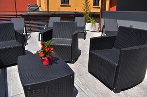 Una terrazza sul tetto con mobili in vimini nero e una pianta in vaso con fiori rossi.