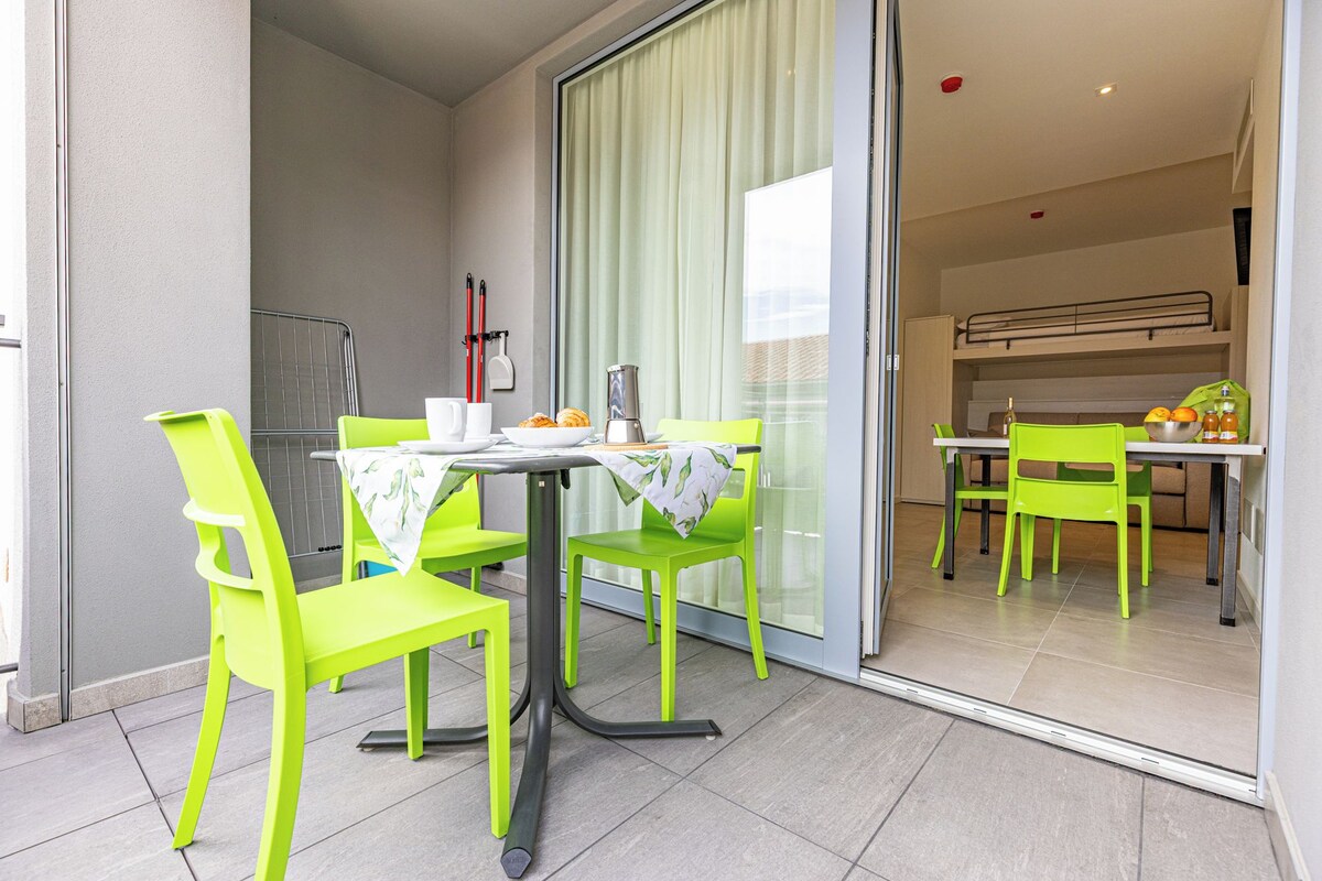 Un coin repas avec une table dressée pour deux personnes, des chaises et une vue sur la cuisine.