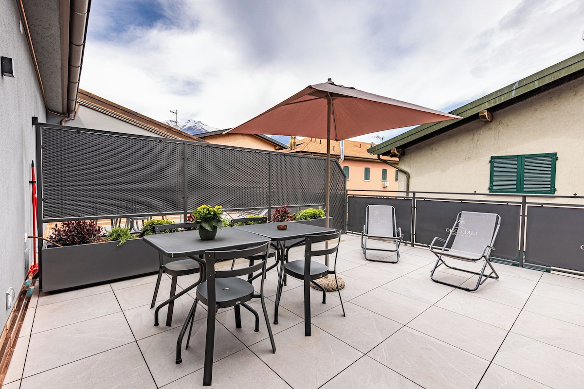 Une terrasse extérieure avec une table et des chaises, une plante en pot et un grand parasol.