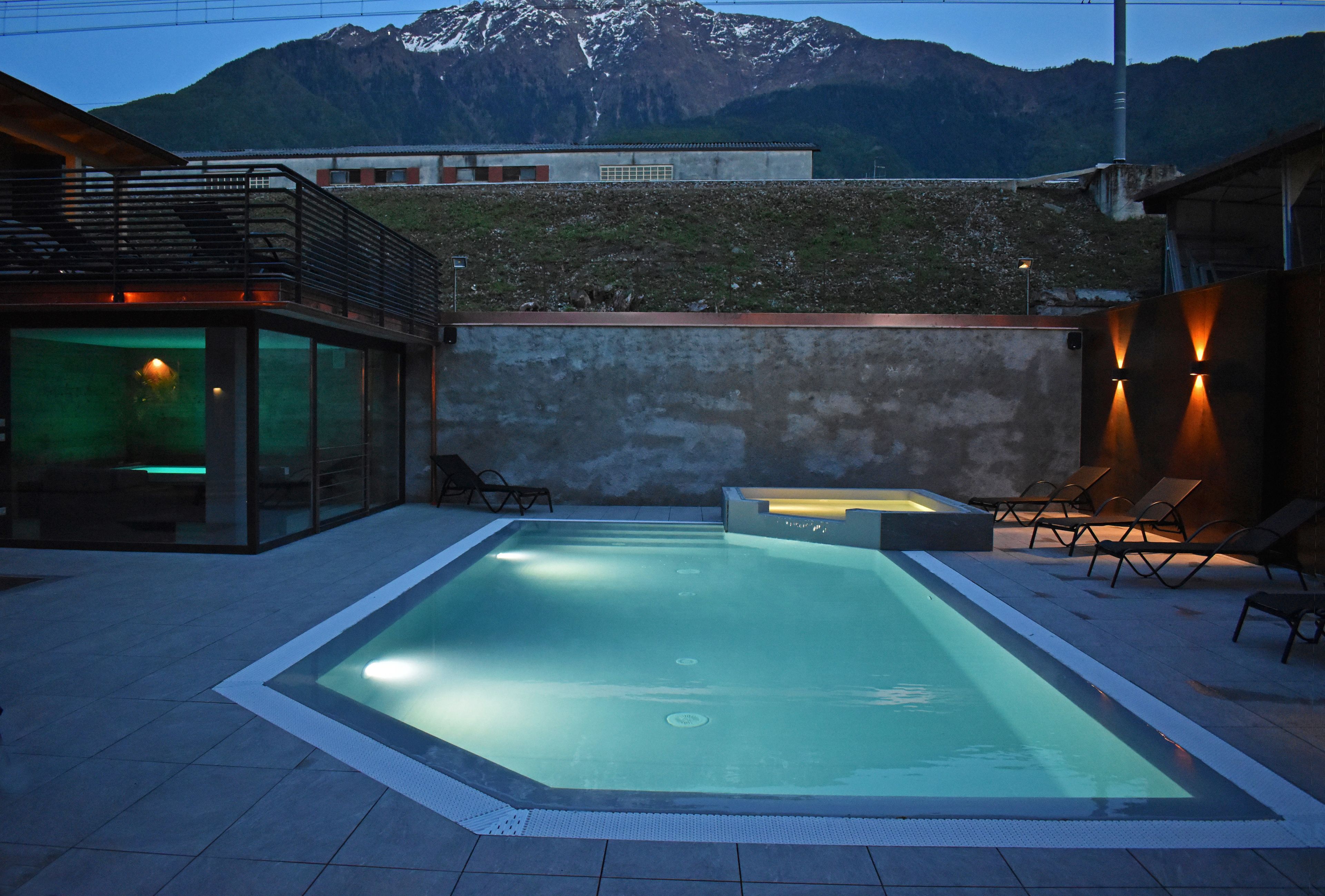 A swimming pool with a view of mountains, a covered seating area, and a modern building with glass walls.