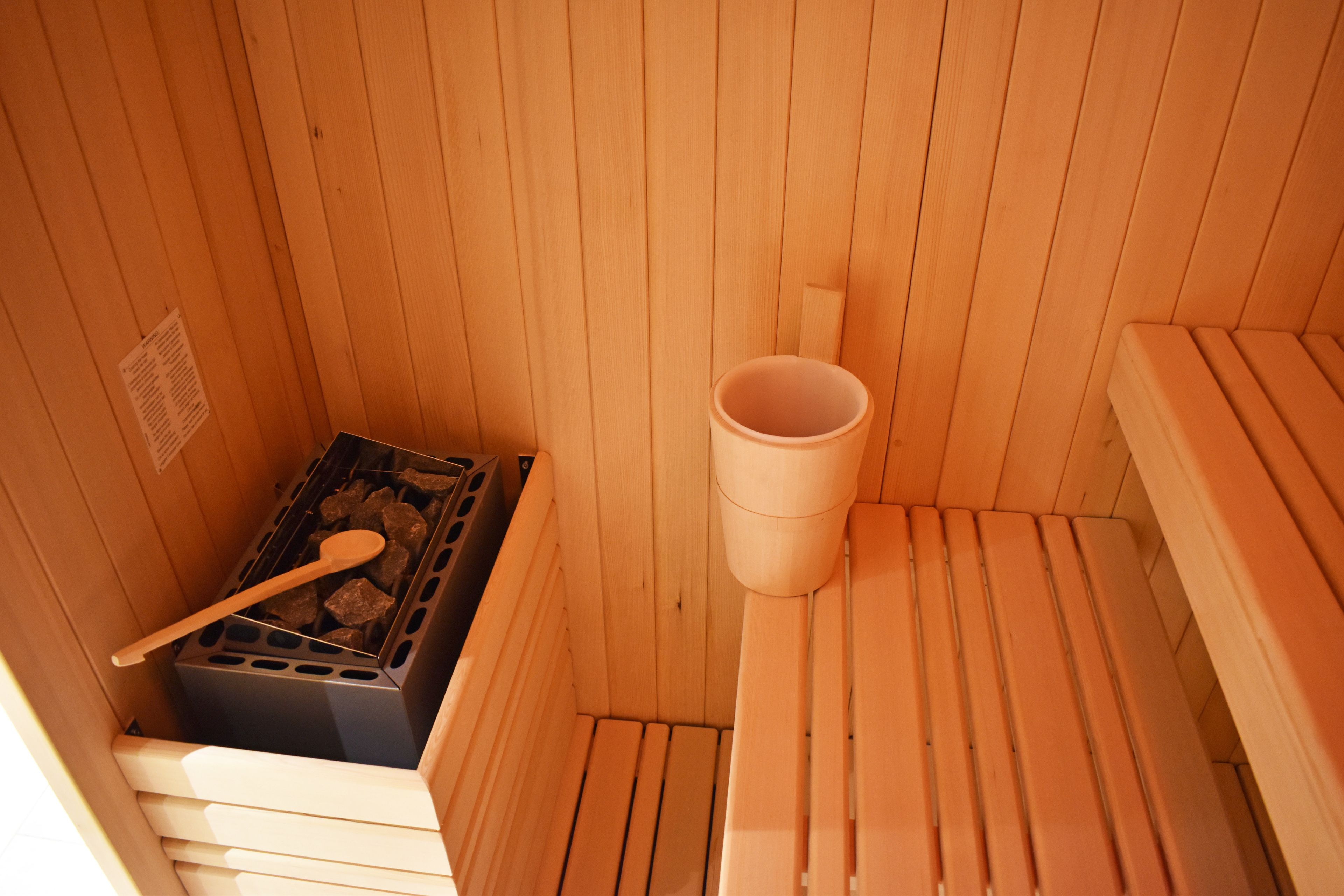 Een houten sauna met banken, een houten emmer en een sauna kachel.