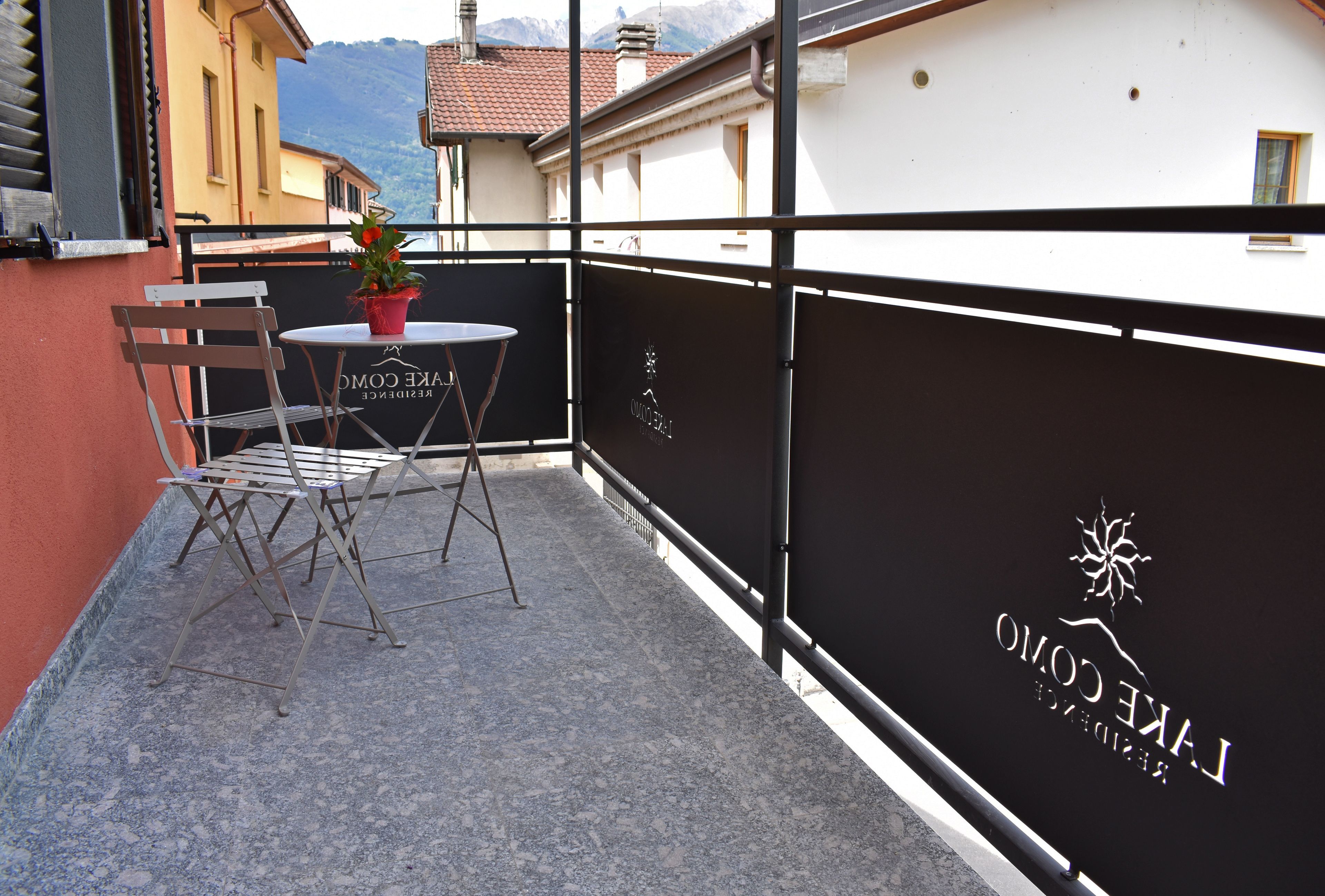 A balcony with a table and chairs, a potted plant, and a sign reading "L'AKCE CROMO."