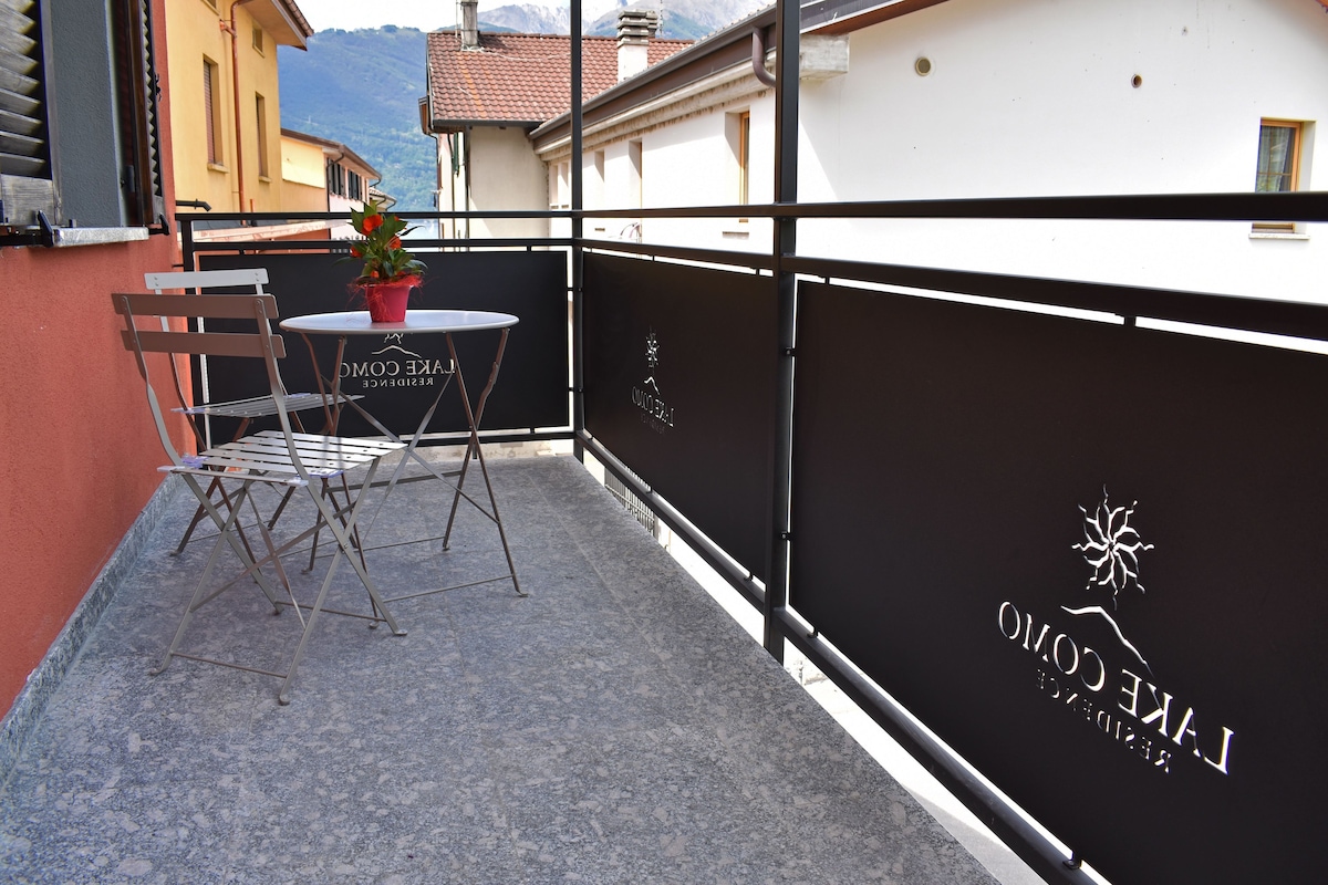 Un balcon avec une table et des chaises, un pot de fleurs et une enseigne sur laquelle on peut lire : « L’AKCE CROMO ».