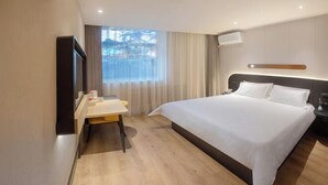 A hotel room with a large bed, a desk, a chair, a TV, and a window with curtains. - Jinjiang Inn (Tianshui)