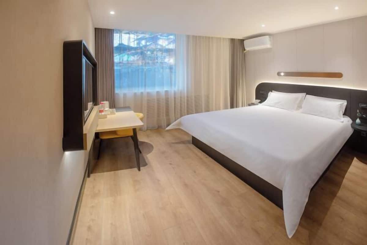 Habitación de hotel con una cama grande, un escritorio, una silla, un televisor y una ventana con cortinas.