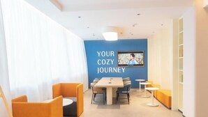 A modern hotel lobby with a blue wall, a television, a table with chairs, and orange seating areas. - Jinjiang Inn (Tianshui)