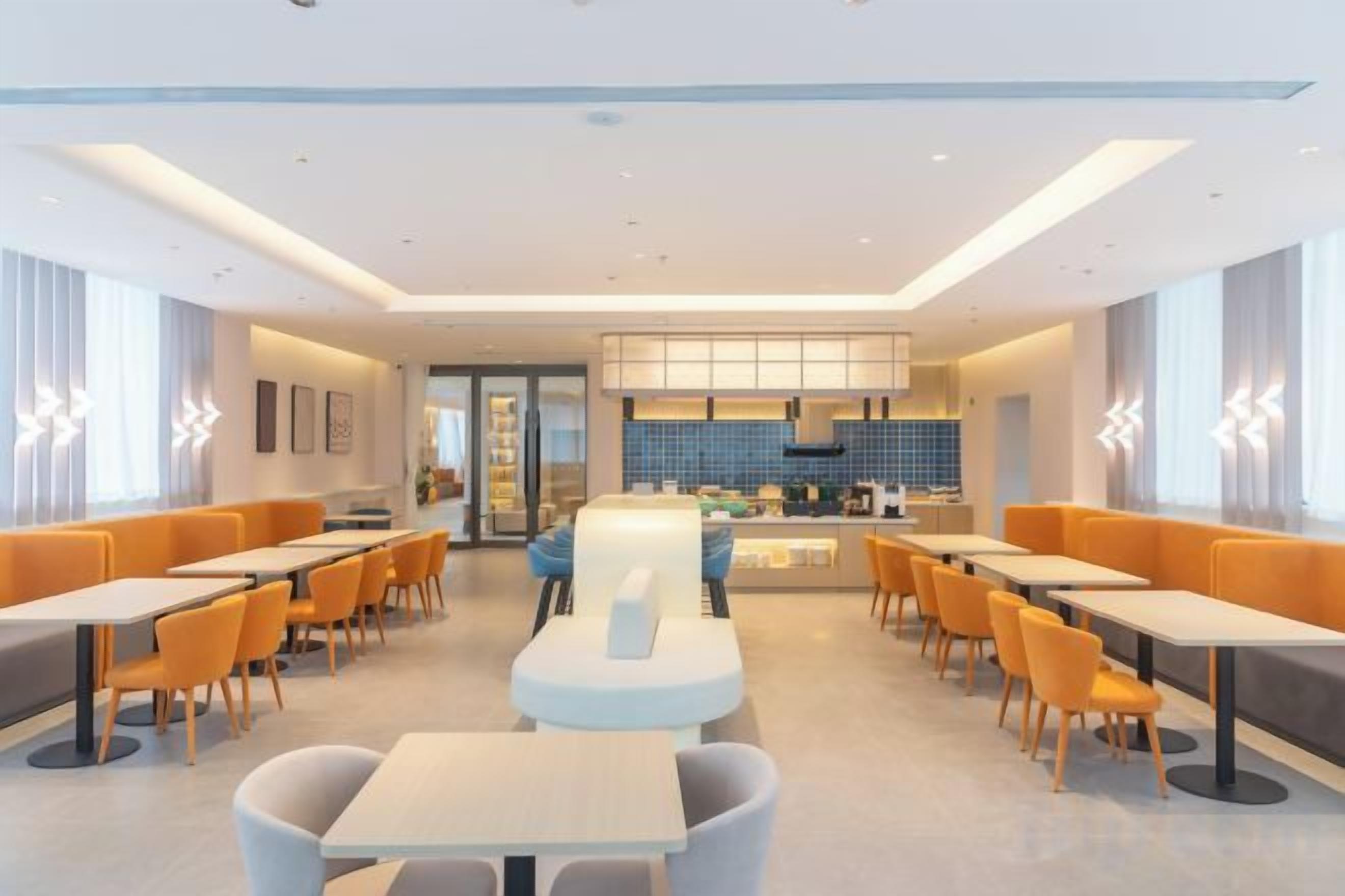 A modern dining area with tables and chairs, a central counter, and a kitchen in the background.