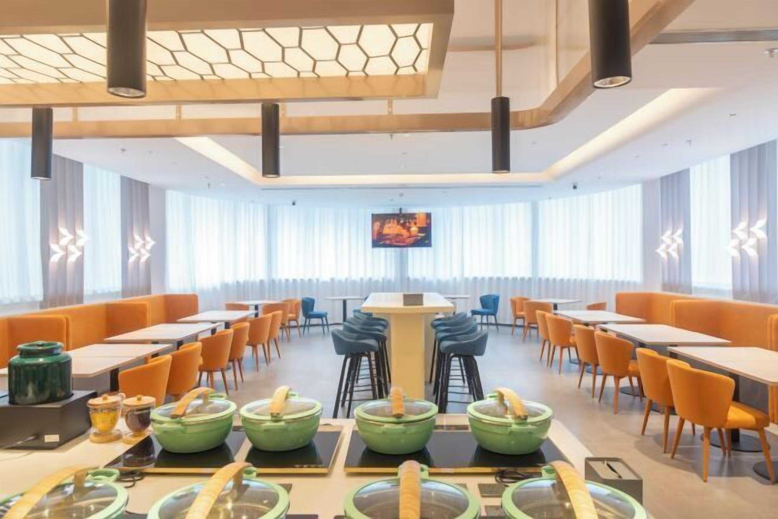 Un espace repas moderne avec des tables et des chaises, un bar central et un grand écran diffusant une vidéo.