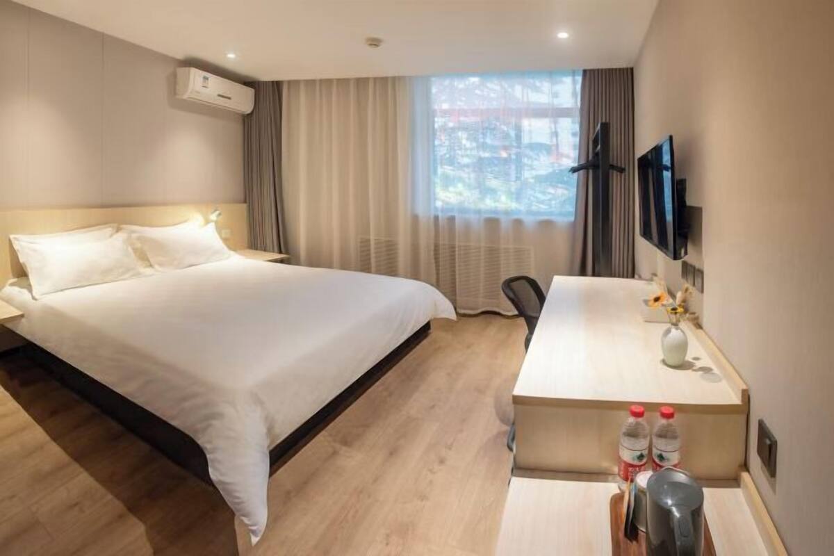 Habitación de hotel con cama, escritorio, silla, televisor y ventana con cortinas.