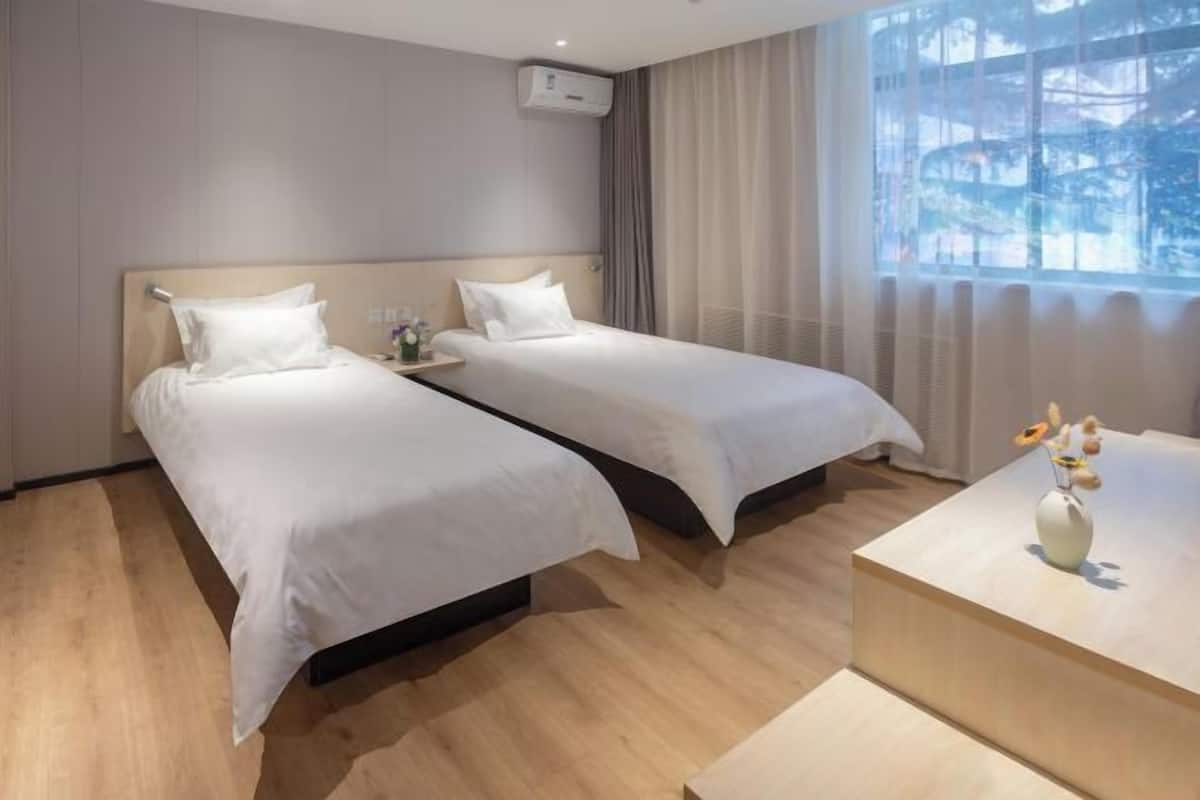 Una habitación de hotel con dos camas, una mesita de noche con un florero y una ventana con cortinas.