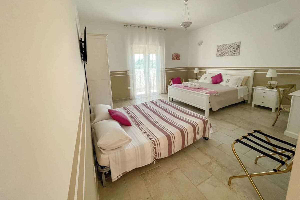 A bedroom with two beds, a small table, a chair, and a window with curtains.