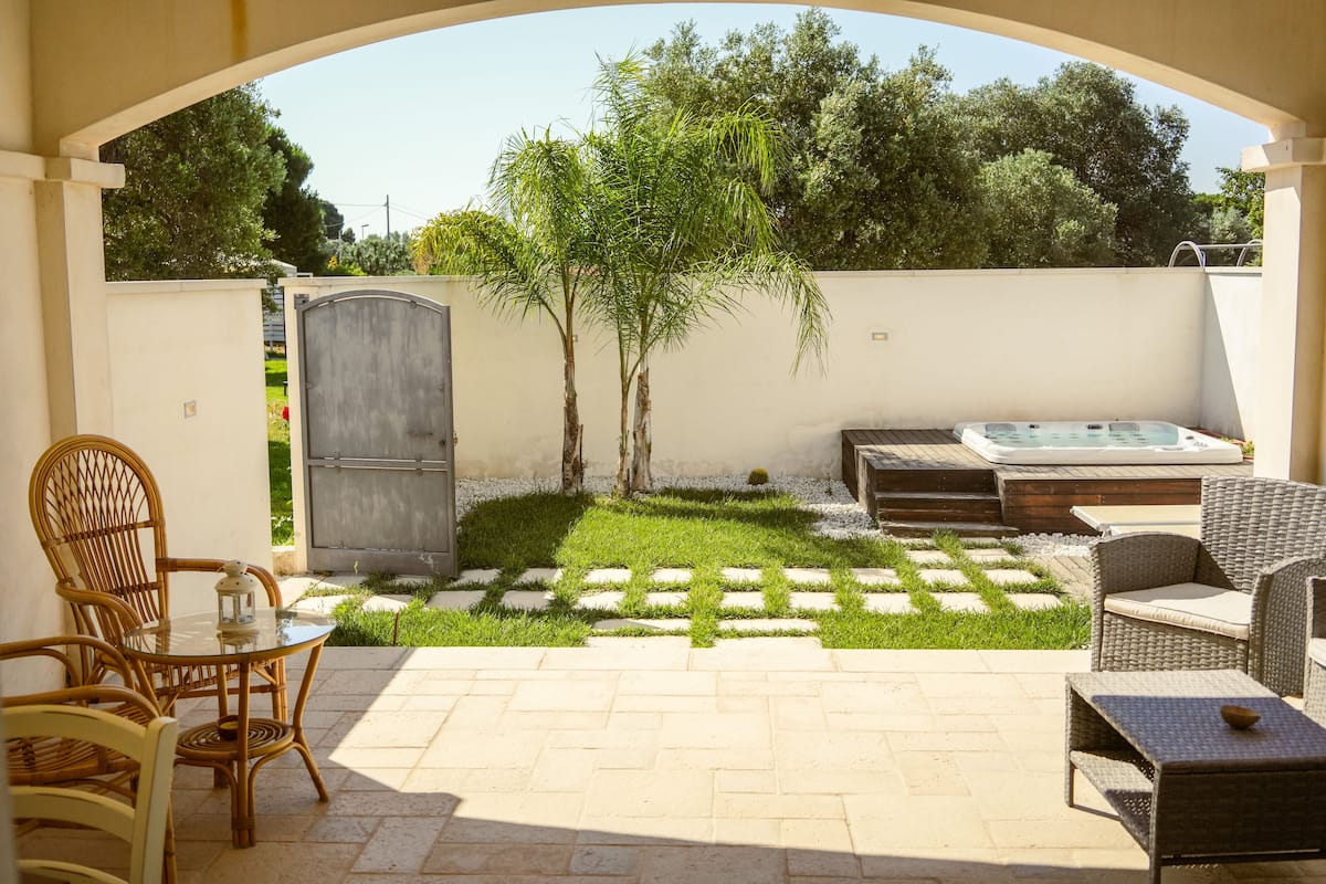 A patio with wicker furniture, a hot tub, and a small lawn area.