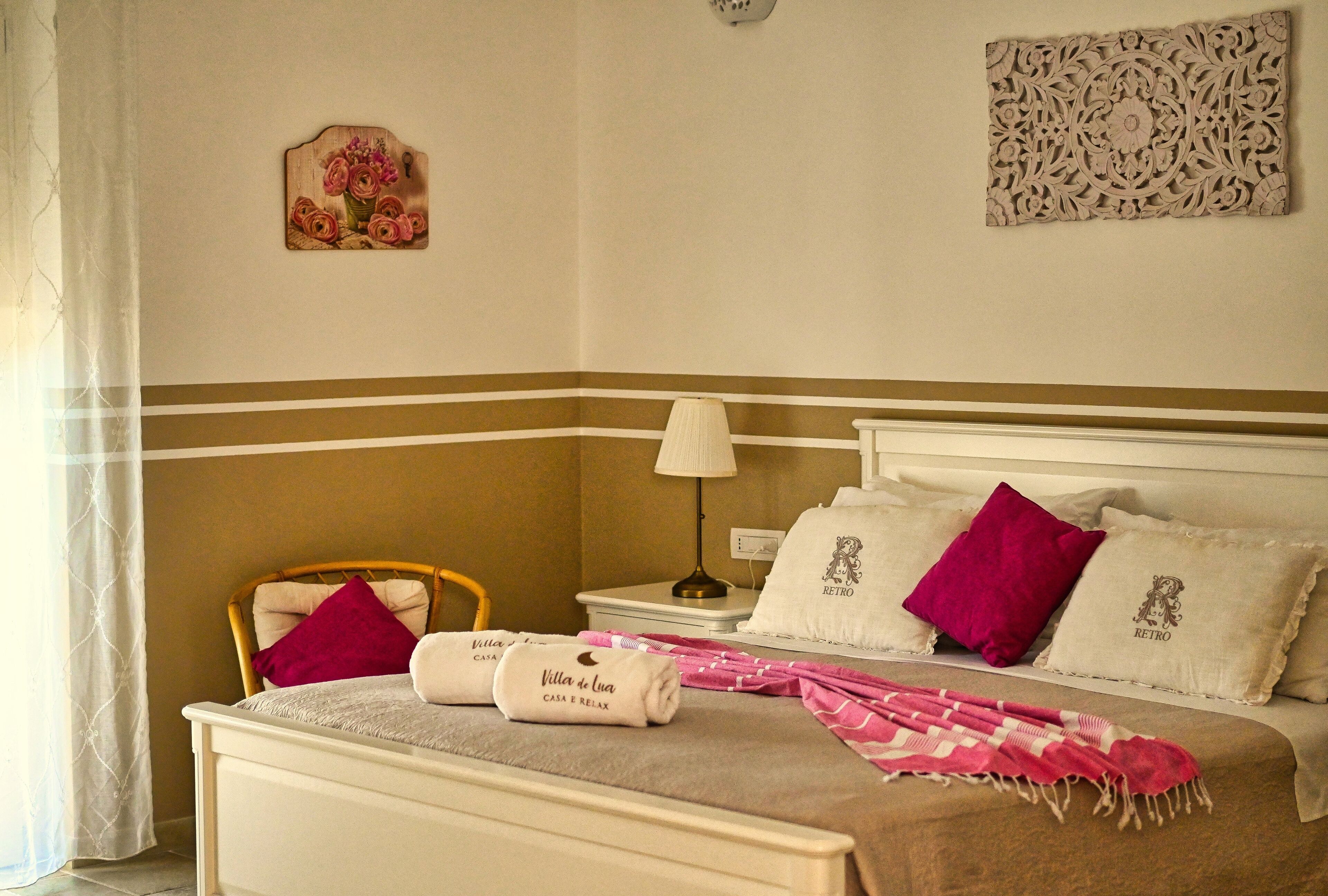 A neatly arranged bedroom with a bed, pillows, a chair, a lamp, and decorative wall art.