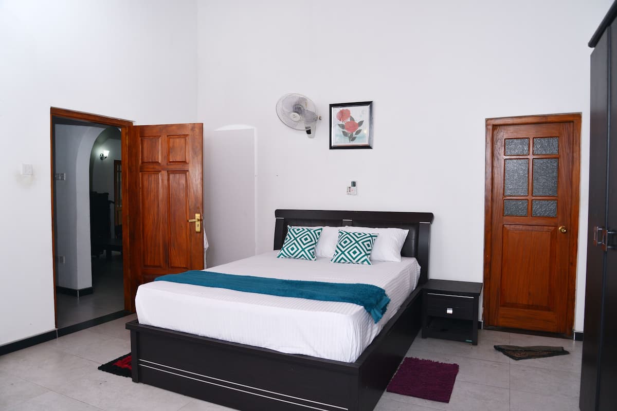 A bedroom with a bed, wooden doors, a bedside table, and a wall-mounted fan.