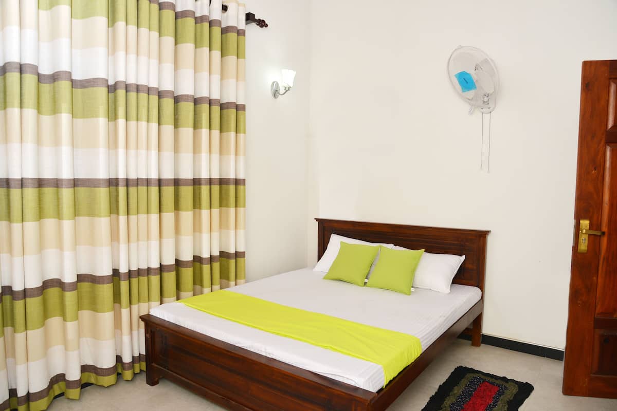 A neatly made bed with a wooden headboard, a green and white striped curtain, and a small wall-mounted fan.