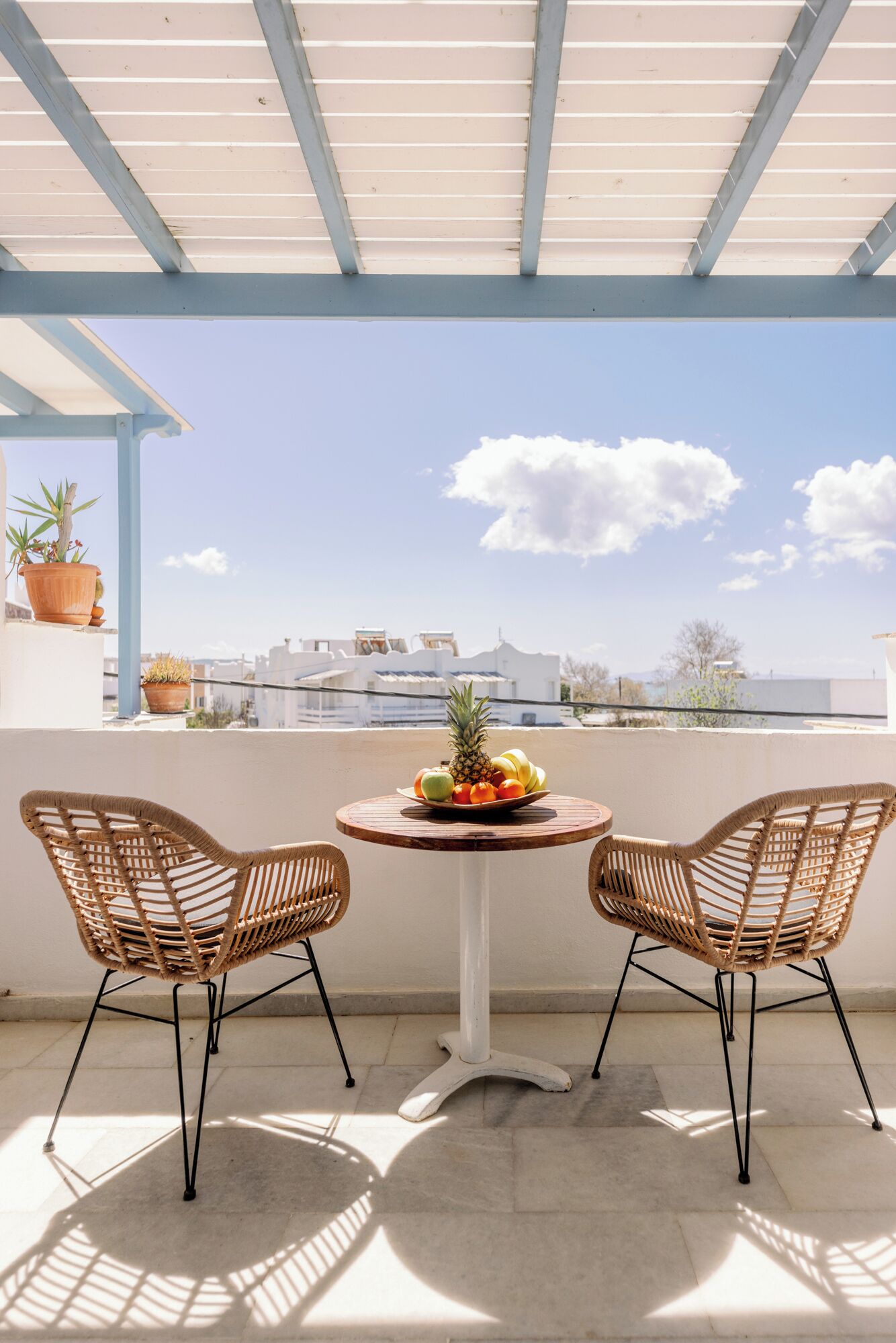 A balcony with two wicker chairs, a small round table with a fruit bowl, and potted plants.