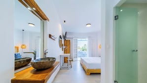 Un bany modern amb un penjador de fusta, un gran lavabo i una porta de vidre per a la dutxa.