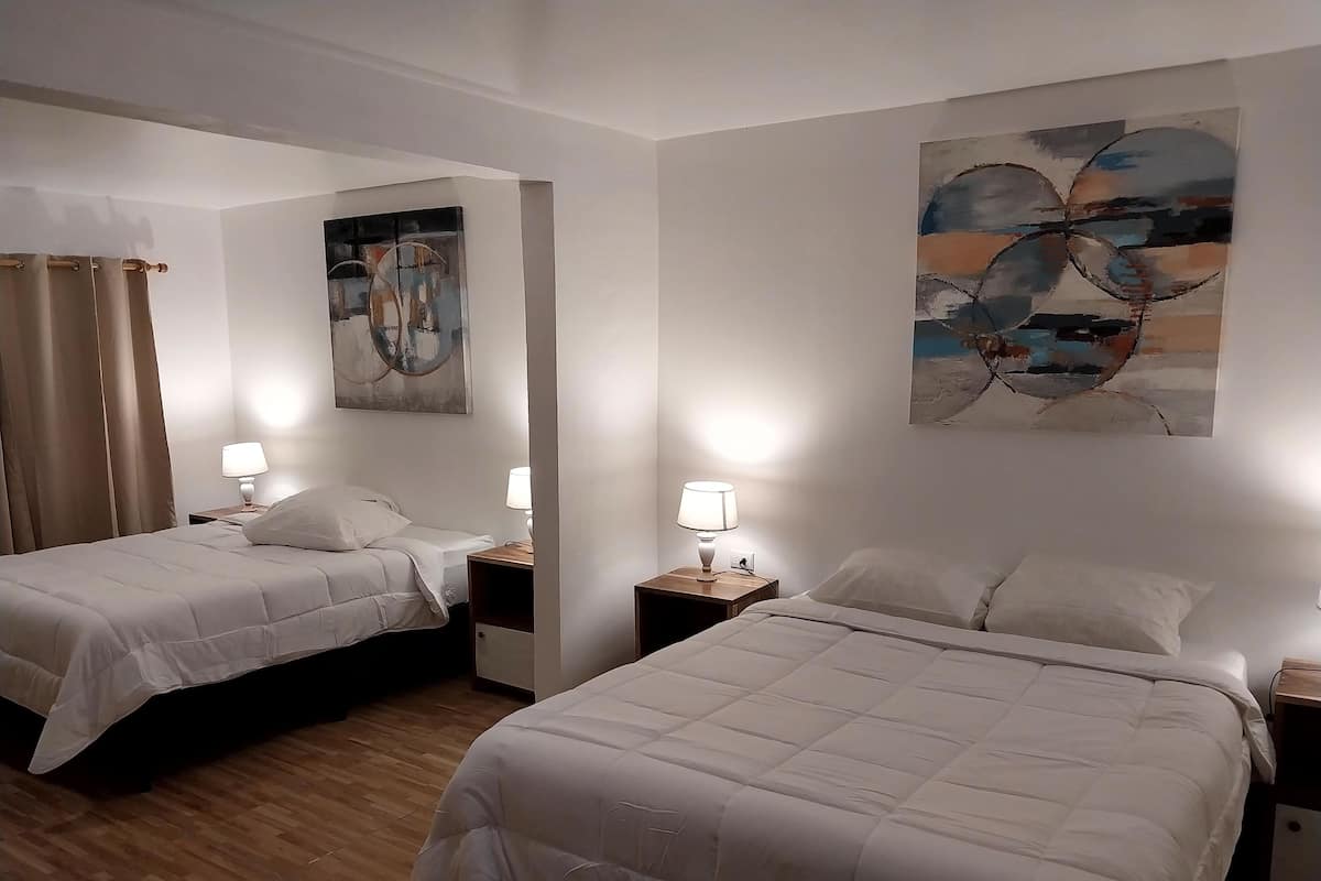 A hotel room with two beds, each with a bedside table and lamp. There are abstract paintings on the walls.
