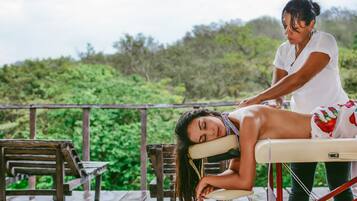 Experience a serene outdoor massage on a tranquil deck surrounded by lush greenery.