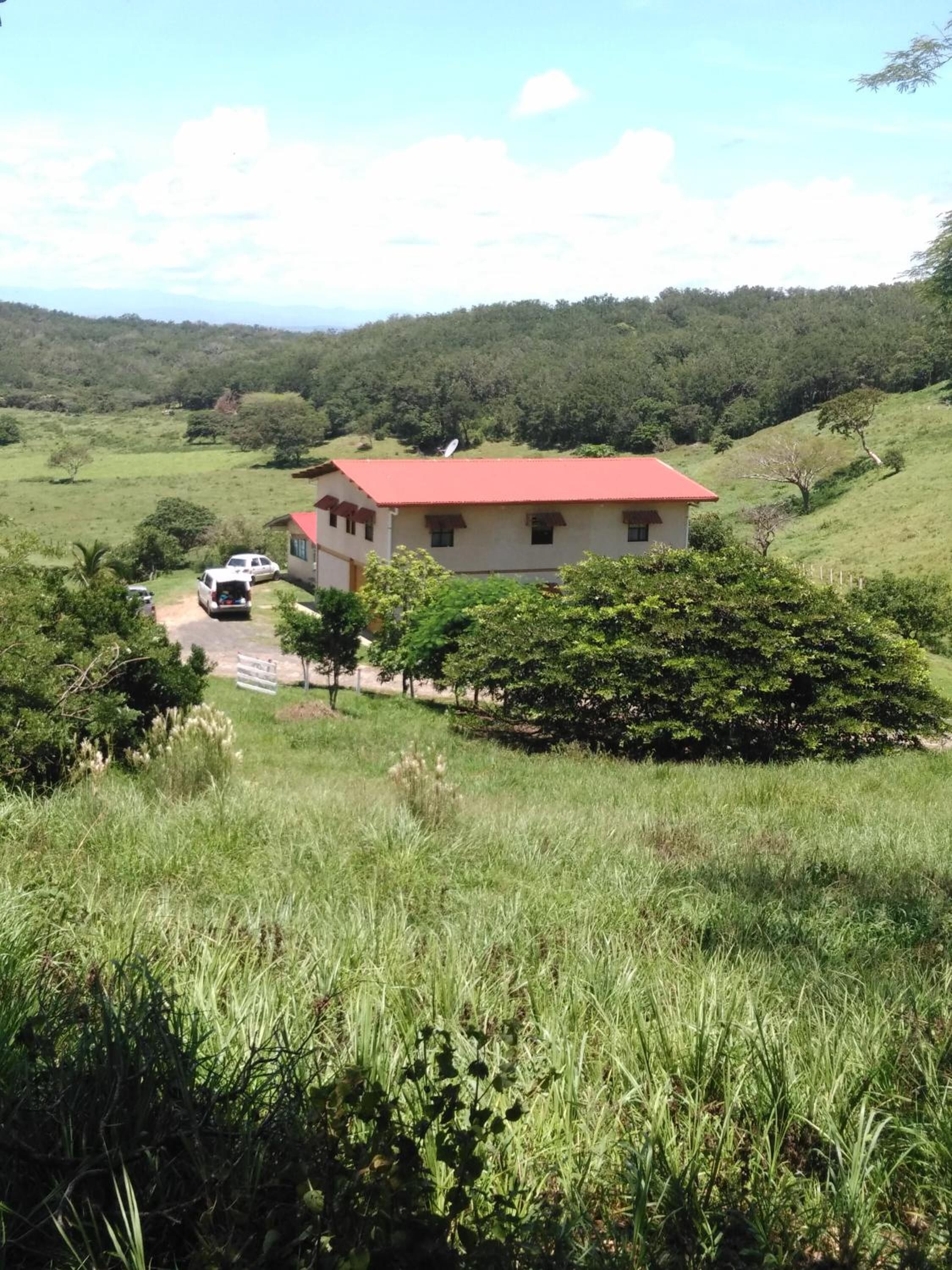 A single-story building with a red roof, surrounded by lush greenery and hills in the background.