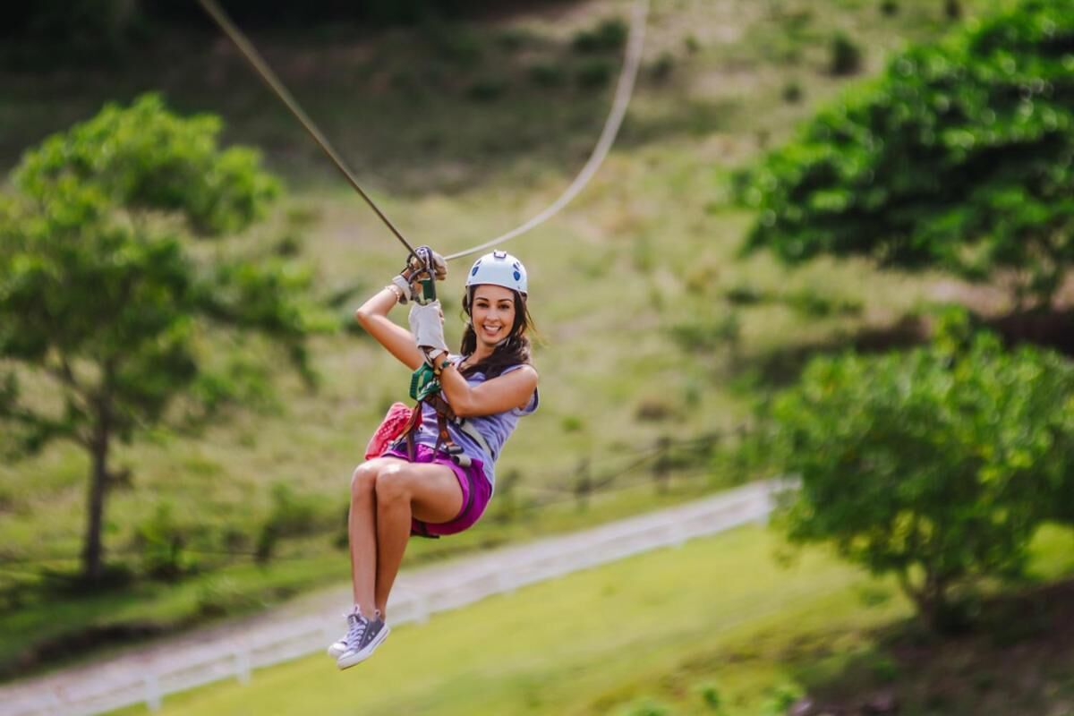 A person ziplining in a natural setting with trees and a path.